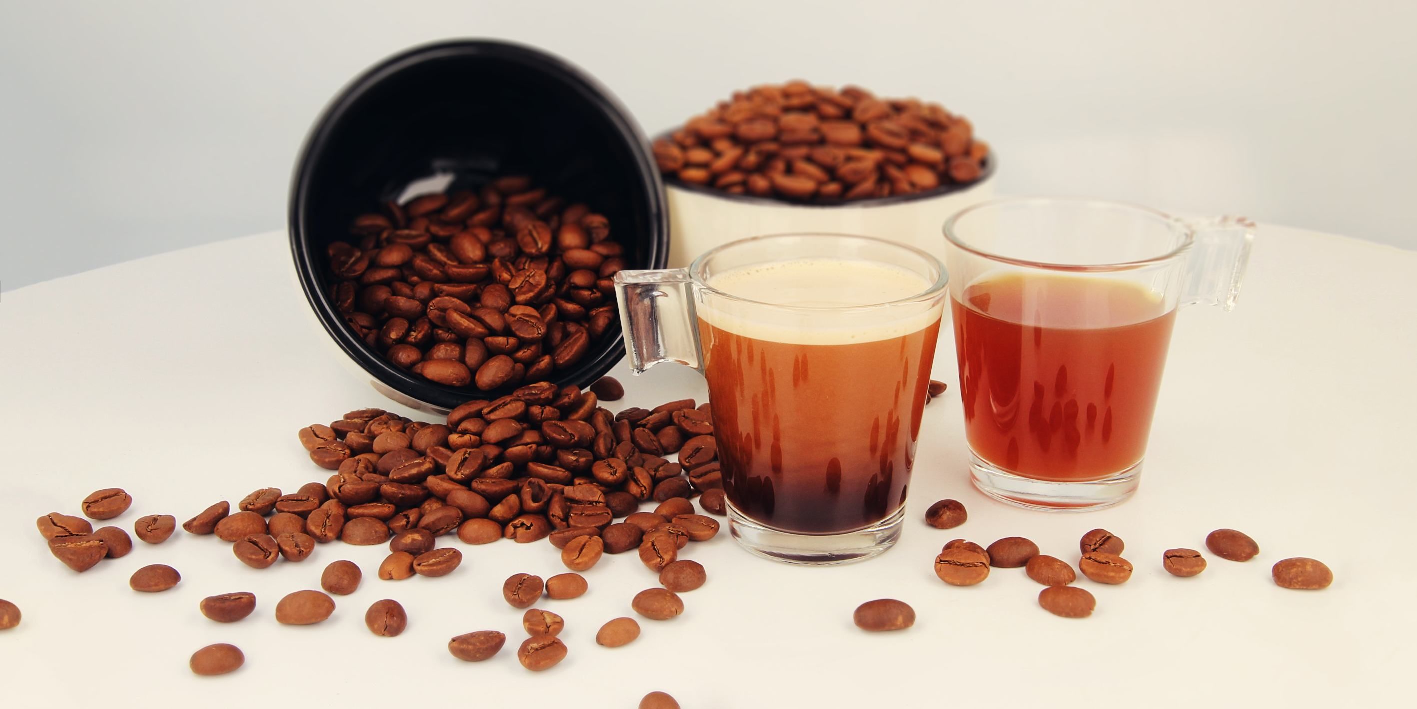Das Bild zeigt zwei Tassen Kaffee und zwei Schüsseln mit Kaffeebohnen