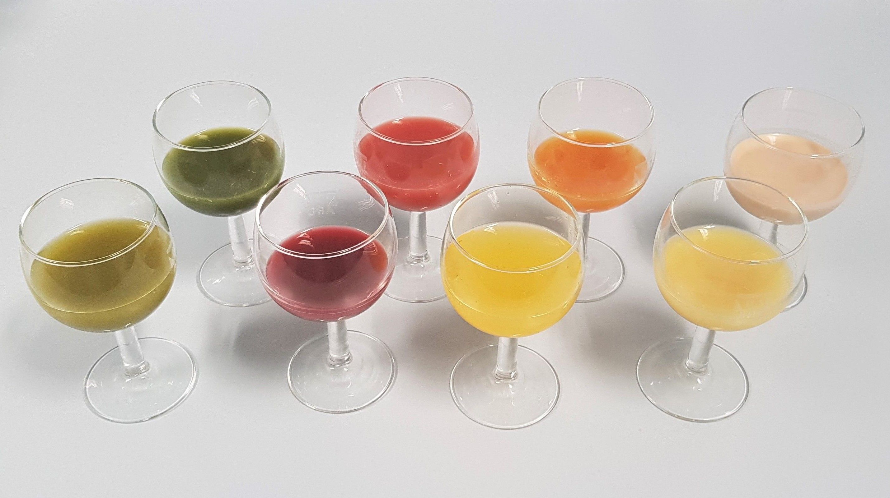 Das Bild zeigt acht Trinkgläser mit verschiedenfarbigen Smoothies gefüllt (vor allem grün, rot, gelb, orange)