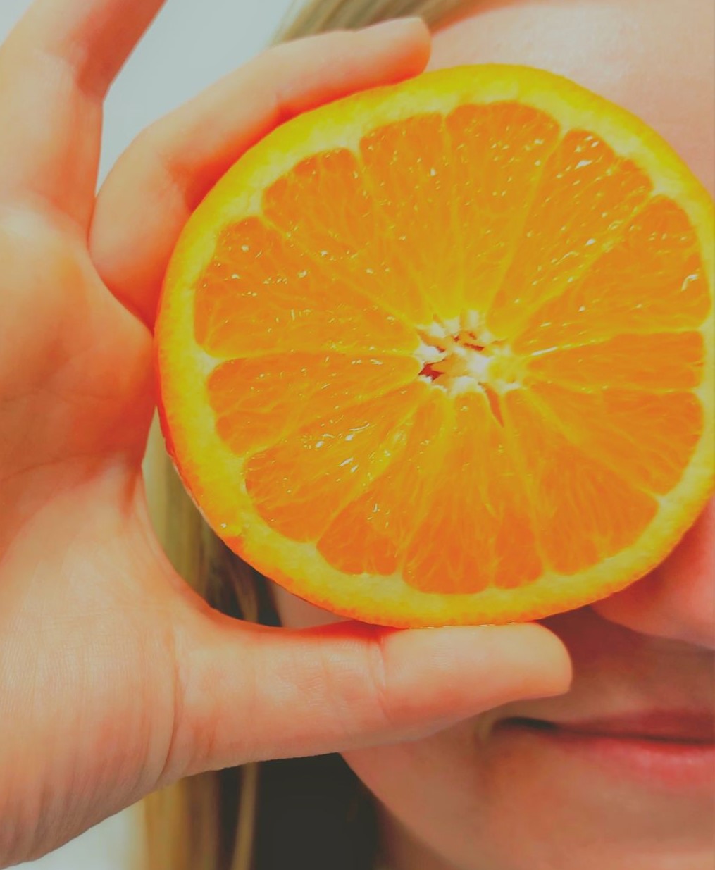 Abgebildet ist eine Person, die sich eine Orangenscheibe vor das Auge hält.