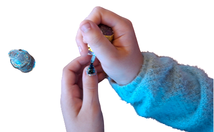 Auf dem Bild sind Kinderhände abgebildet. Die eine hält den Pinsel eines blau-glitzernden Nagellackes und trägt den Nagellack auf den Daumen der anderen Hand auf. Im Hintergrund steht der Nagellack