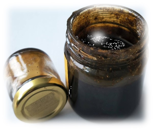 Das Bild zeigt ein geöffnetes Honigglas mit dunkelbrauner, zäher Paste und danebenliegend ein Glas mit Schraubdeckel.